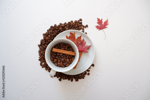 Roasted coffee beans composition with cinnamon sticks and maple leaves on white background. Seasonal drink image concept background.  photo