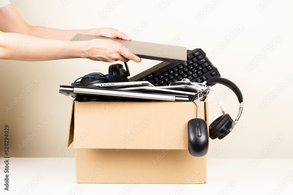 Woman hands put old laptop computer in cardboard box full used
