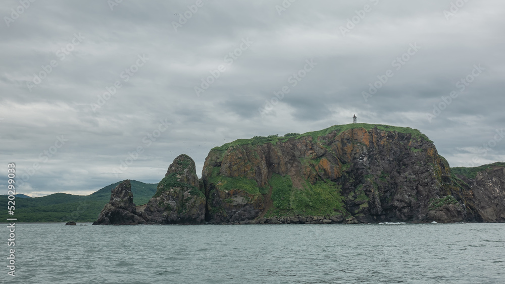 Sheer cliffs of the Kamchatka coast against a cloudy sky. Green hills in the distance. Avacha Bay Sheer cliffs of the Kamchatka coast against a cloudy sky. Green hills in the distance. Avacha Bay