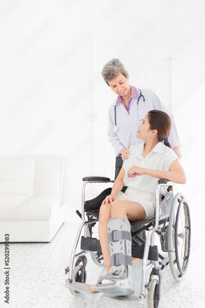 Asian doctor drive wheelchair of patient, patient wear aircast walking boot, doctor and patient talk about symptoms and treatment plan, rehabilitation activity Asian doctor drive wheelchair of patient, patient wear aircast walking boot, doctor and patient talk about symptoms and treatment plan, rehabilitation activity