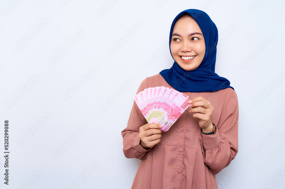 Smiling young Asian muslim woman in pink shirt holding money banknotes ...