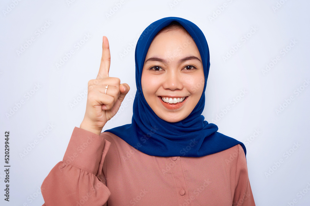 Excited young Asian muslim woman in pink shirt pointing finger up at copy space isolated over white background. People religious lifestyle concept Excited young Asian muslim woman in pink shirt pointing finger up at copy space isolated over white background. People religious lifestyle concept