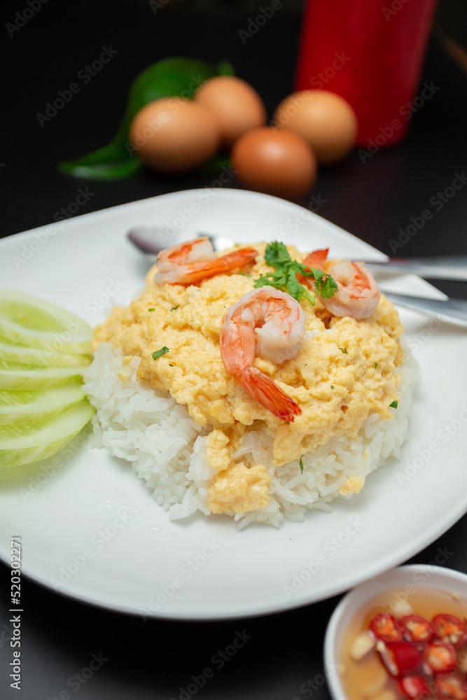 Close-up scrambled egg rice on top with shrimp in a white plate placed on a wooden table .Fast food, breakfast