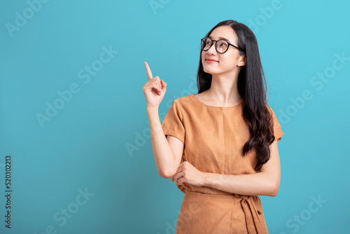 Happy Portrait smiling young asian woman isolated on blue background , Beautiful asian female pointing finger upward on blue background