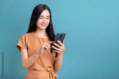 Happy Portrait smiling young asian woman using smartphone isolated on blue background