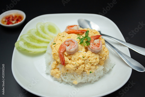 Close-up scrambled egg rice on top with shrimp in a white plate placed on a wooden table .Fast food, breakfast