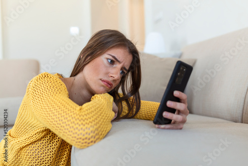 Tablou canvas Pensive sad young woman holding smartphone waiting sms from boyfriend