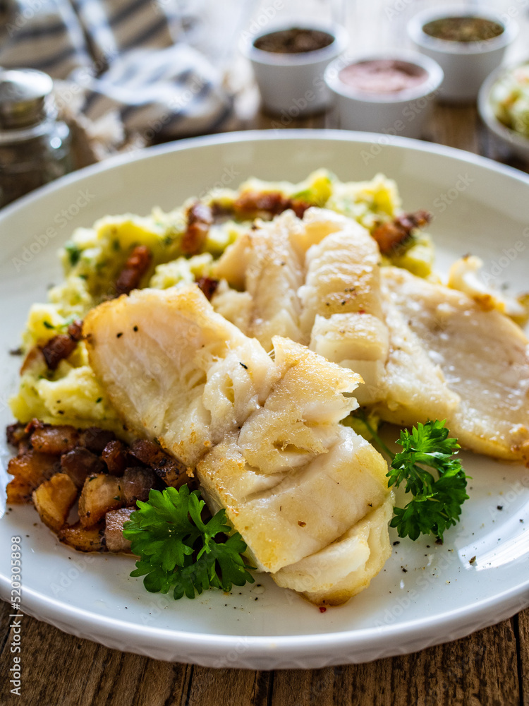Fish dish - fried cod fillet with potato puree and bacon on wooden table
Fish dish - fried cod fillet with potato puree and bacon on wooden table