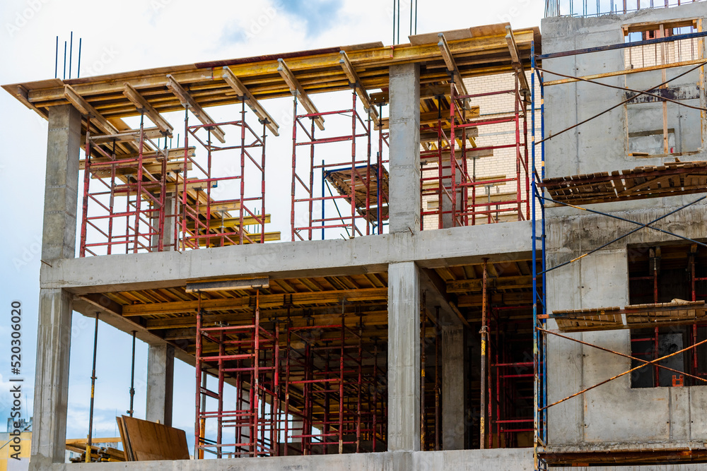 Construction of a new monolithic reinforced concrete house. Scaffolding on the facade of a building under construction. Working at height on a construction site.