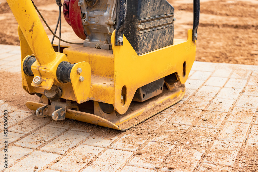 Vibratory rammer with vibrating plate on a construction site. Compaction of the soil before laying paving slabs. Close-up.