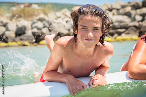 Fotografie, Obraz Handsome teenage boy lying on a swimming board and having fun floating on a swim