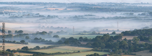 Glorious landscape image of layers of mist rolling over South Downs National Park English countryside during misty Summer sunrise