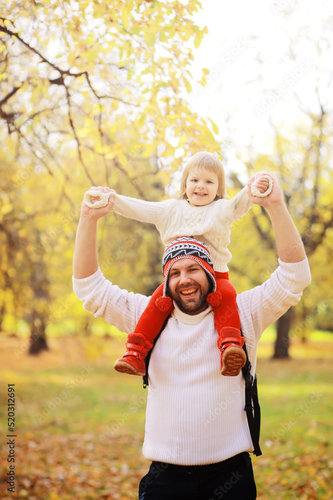 Fototapeta premium Young family on a walk in the autumn park on a sunny day. Happiness to be together.