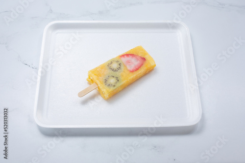 A view of a pineapple orange mango paleta, featuring slices of kiwi and strawberry. photo