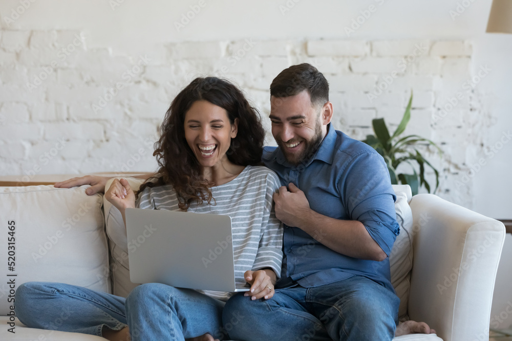 Excited millennial married couple looking at laptop computer screen with winner yes hands, laughing, shouting for joy, celebrating success, achieve, winning prize, money, learning good happy news Excited millennial married couple looking at laptop computer screen with winner yes hands, laughing, shouting for joy, celebrating success, achieve, winning prize, money, learning good happy news