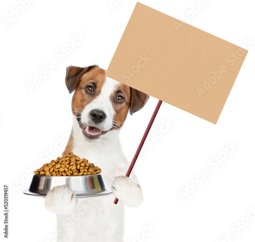 Jack Russell Terrier puppy holds bowl of dry dog food and shows empty placard. isolated on white background © Ermolaev Alexandr