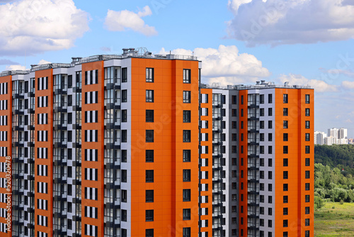 Photography New residential buildings with orange lining on background of green park and blue sky with white clouds