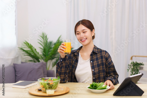 Lifestyle in living room concept, Asian woman drinking orange juice and eating vegetable salad