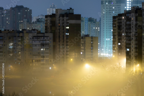 Night cityscape of the big city. Awesome bright  multi colored light in thick fog at empty streets. Apartment buildings in bedroom community  commuter town area. Darnytsia  Kyiv. Ukraine. 2021