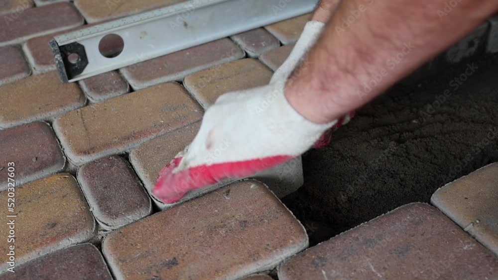 Builder. The hands of a master mason lay paving slabs. Hands of the master in gloves, the process of laying paving stones in layers, sealing with a mallet. Slow Motion, Low Angle. Builder. The hands of a master mason lay paving slabs. Hands of the master in gloves, the process of laying paving stones in layers, sealing with a mallet. Slow Motion, Low Angle.