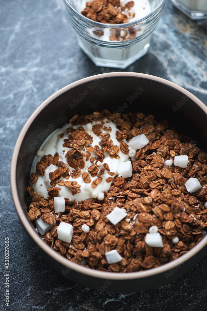 Bowl of chocolate granola with coconut and greek yogurt, vertical shot on a black marble surface, closeup Bowl of chocolate granola with coconut and greek yogurt, vertical shot on a black marble surface, closeup