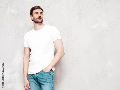Portrait of handsome confident stylish hipster lambersexual model. Sexy man dressed inT-shirt and jeans. Fashion male isolated on grey wall in studio