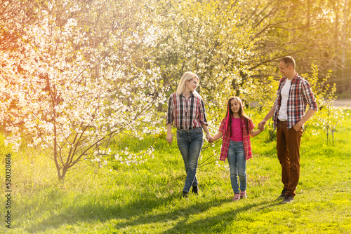 Outdoor portrait of happy young family playing in spring park under blooming tree, lovely couple with little child having fun in sunny garden © Angelov