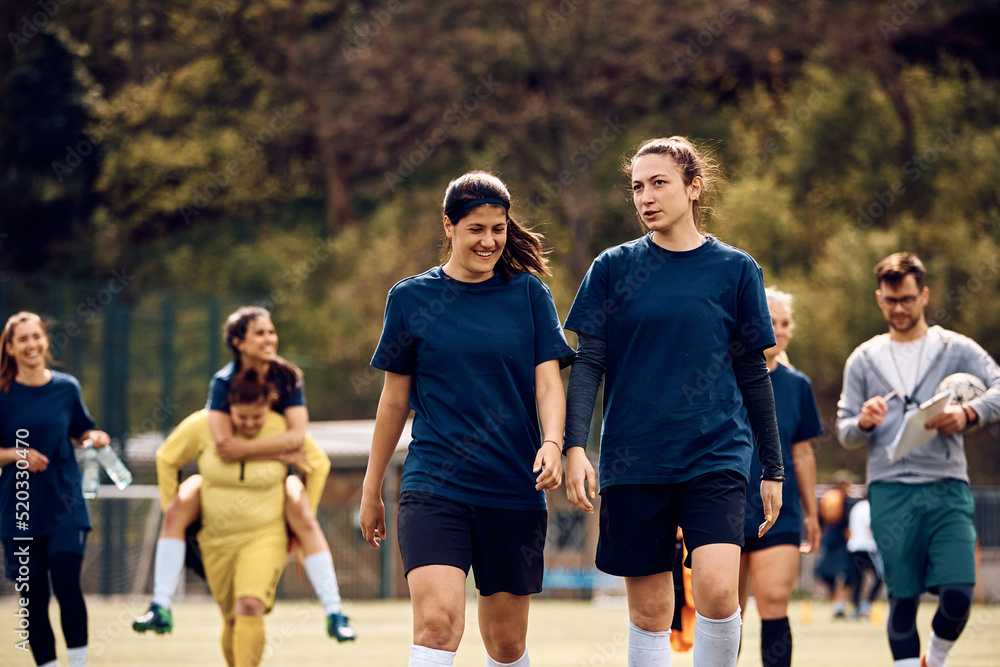 Athletic women communicating while leaving playing field after soccer training.