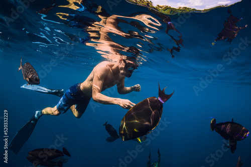 Freediver with fins and mask swim with school of big fish in blue ocean