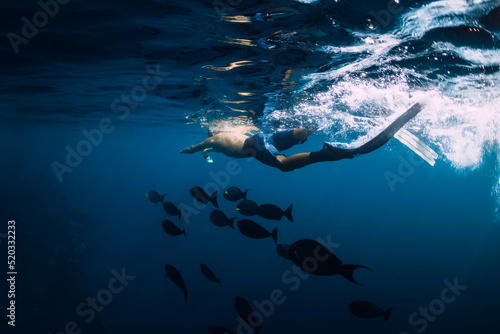 Freediver with school of fish swim in tropical ocean