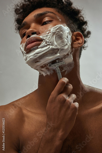 Partial of african american guy shaving with razor photo