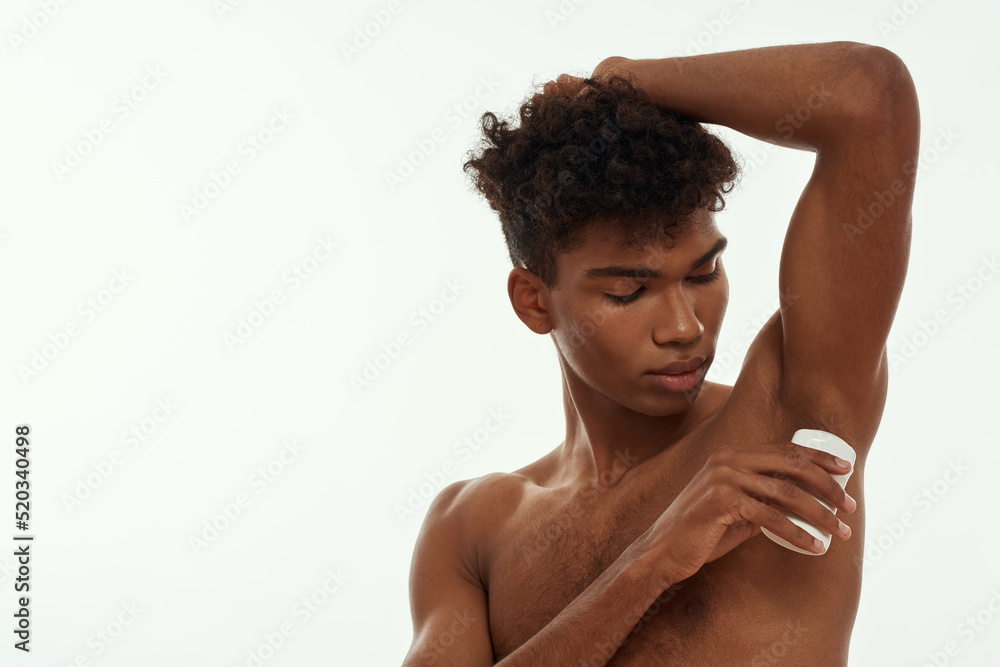 Obraz premium Young black guy applying deodorant on his armpit