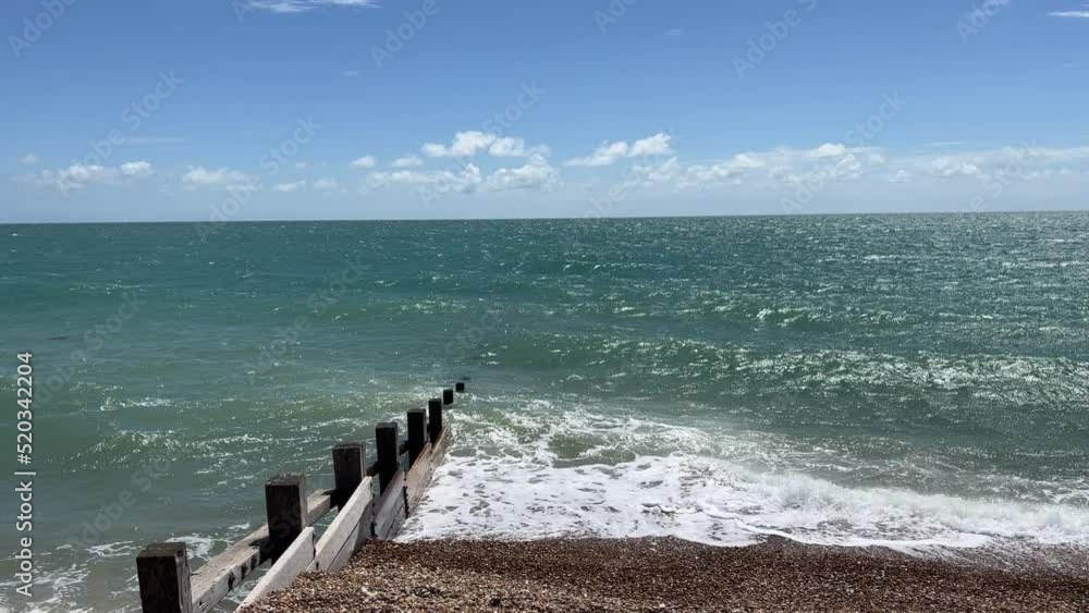 Static camera on the strong waves with white foam of the sea a british south coast town near brighton. View of the beach of pebbles or rocks ,bright blue sea and sky, sunny day. Summer day in Britain. Static camera on the strong waves with white foam of the sea a british south coast town near brighton. View of the beach of pebbles or rocks ,bright blue sea and sky, sunny day. Summer day in Britain.