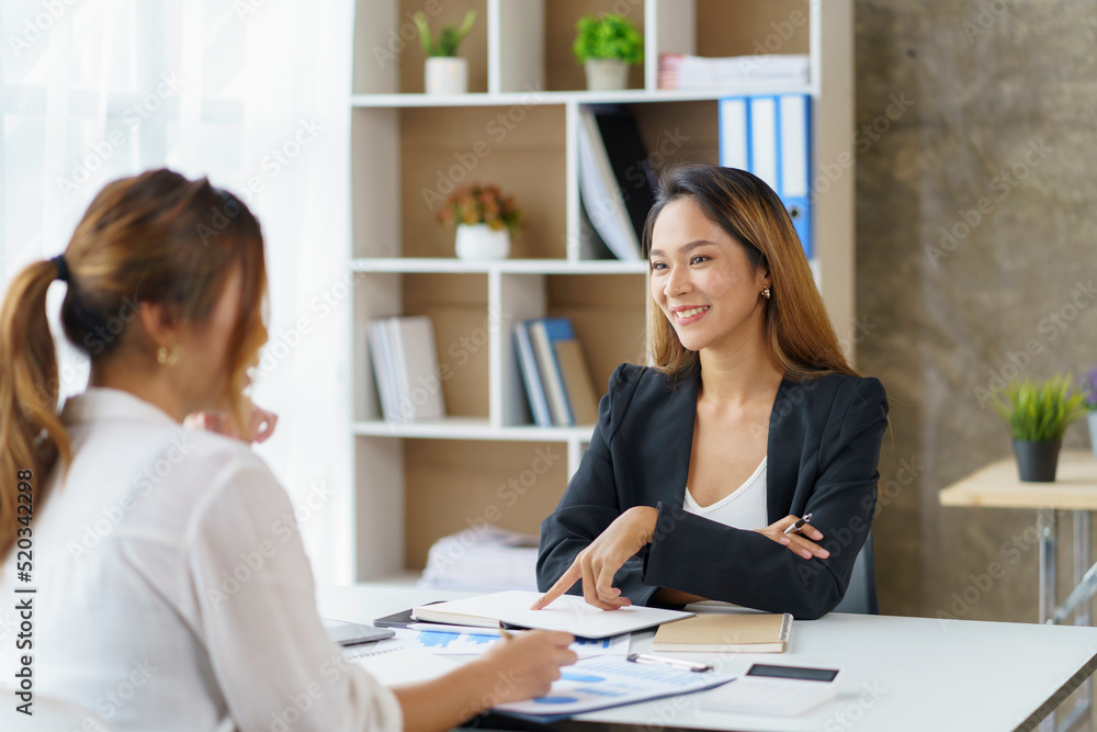 Two young Asian businesswomen discuss the concept of a new start-up project. Analyze marketing planning and financial statement at the office. Two young Asian businesswomen discuss the concept of a new start-up project. Analyze marketing planning and financial statement at the office.