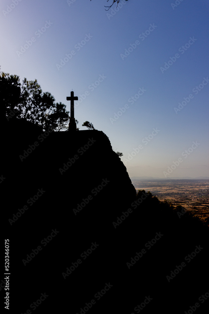 cross on the mountain in shadow siluette with green landscape, San salvador cross, Mallorca, Spain