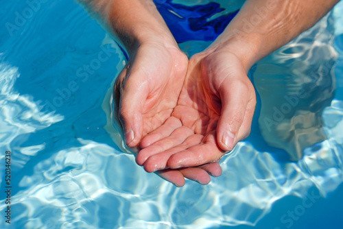 The hands cupped together submerged in clean clear blue water in swimming pool