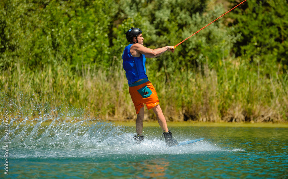 A professional wakeboarder rides on the lake in sunny weather, performing figures A professional wakeboarder rides on the lake in sunny weather, performing figures