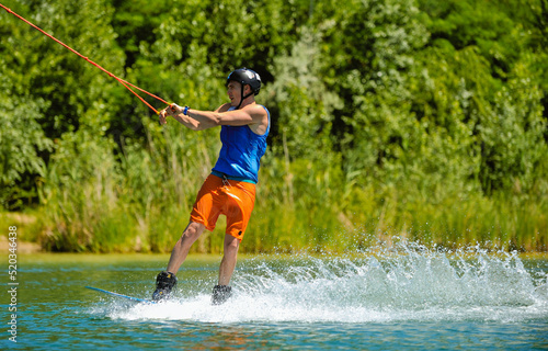 A professional wakeboarder rides on the lake in sunny weather, performing figures