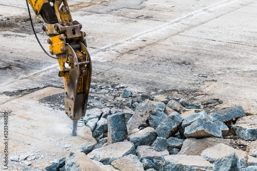 Excavator mounted hydraulic jackhammer at breaking concrete area. Closeup of working demolition hammer with point bit. Heavy equipment detail on construction site. Carpark renewing. Civil engineering.