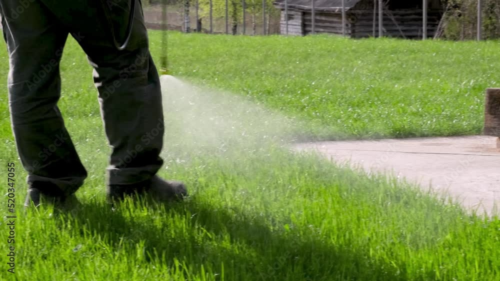 Farmer spraying pesticide on lawn field wearing protective clothing. Treatment of grass from weeds and dandelion. Pest control. Insecticide sprayer with a proper protection. Gardening care season.