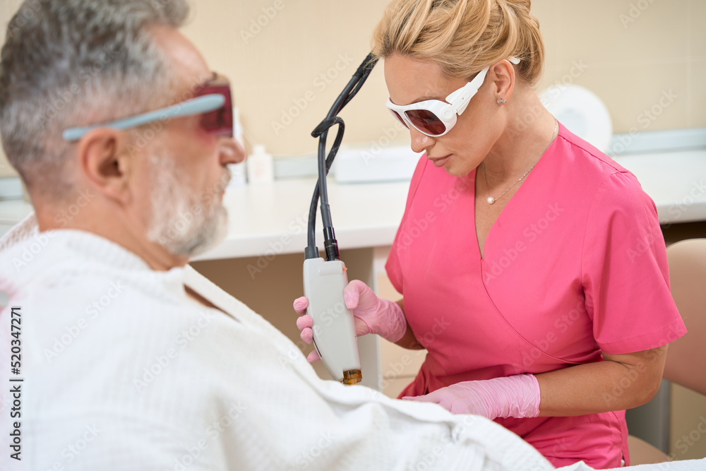 Woman dermatologist doing laser hair removal to man on arm Woman dermatologist doing laser hair removal to man on arm