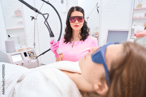 Cosmetologist is holding laser hair removal machine next to client