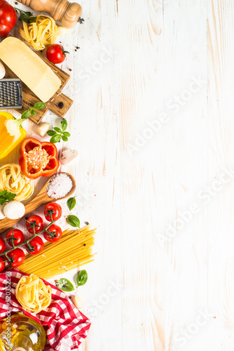 Pasta ingredients on white kitchen table. Raw Pasta, parmesan, olive oil, spices, tomatoes and basil. Top view image with copy space.