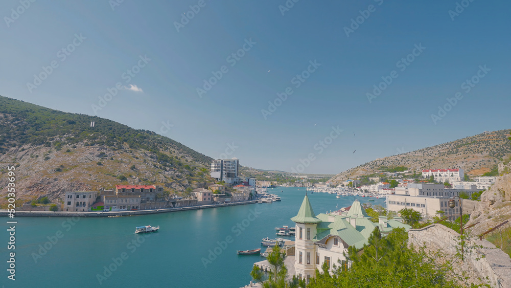 Beautiful bay with boats on background of mountains and city. Action. Mountain coast with clear water and tourist city. Sea city on mountain coast with blue water