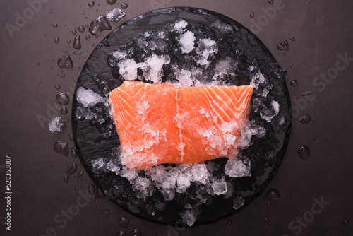 Fresh raw salmon fish steak on a chipped ice over dark stone background