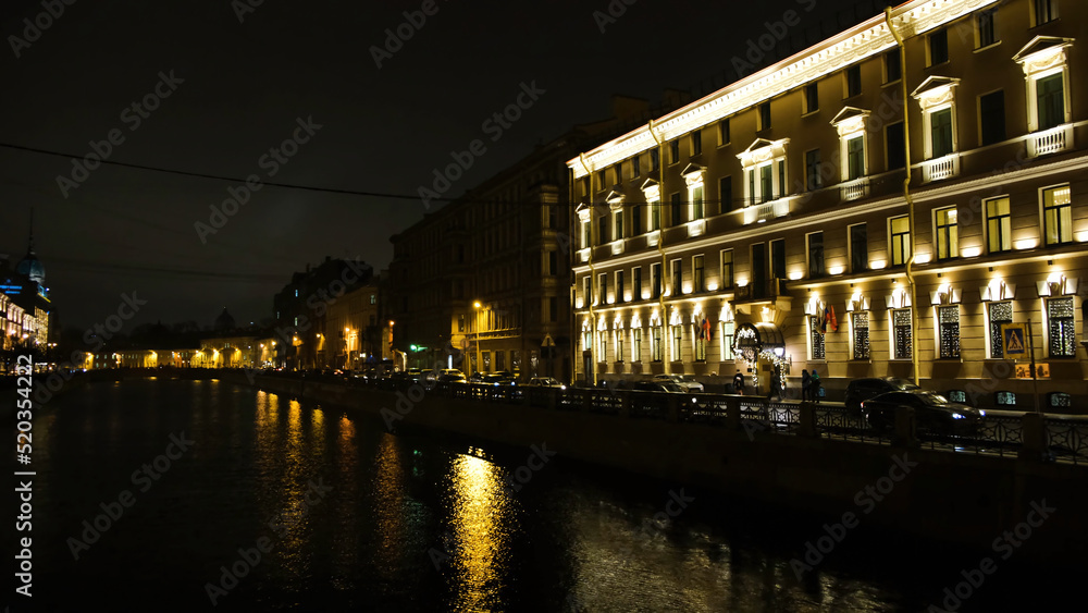 Beautiful view of city canal with evening lights. Concept. Yellow city lights illuminating the streets by canal reflected in water. Beautiful night city in light of lanterns and garlands by canal