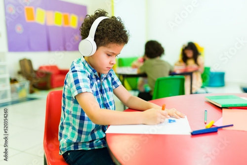 Autistic preschooler with headphones coloring alone in class photo