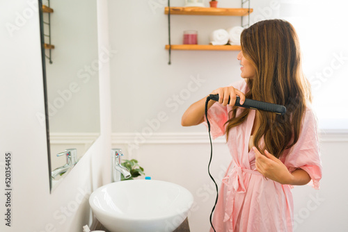 Mexican young woman straightening her hair with an iron photo