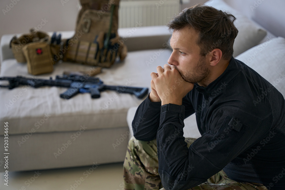 Soldier sitting next to bed with his gun and equipment