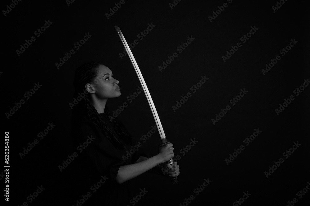 Beautiful curly woman with a katana sword in darkness in black and white Beautiful curly woman with a katana sword in darkness in black and white